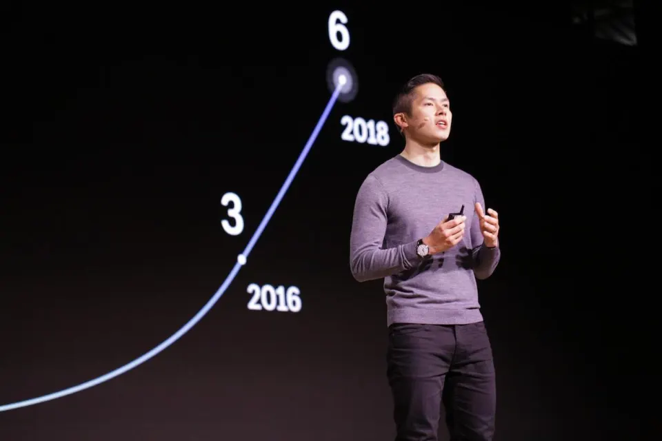 Brandon giving a keynote on a dark stage, with a growth chart behind him